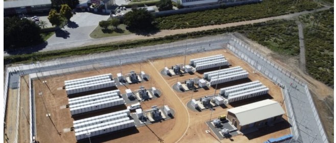 Aerial view of a battery storage site in South Africa with rows of white battery containers, inverters and a substation